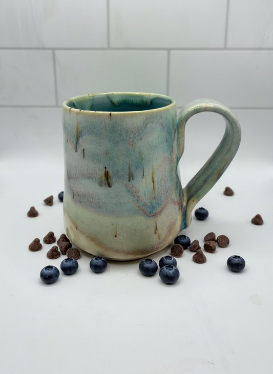 Handmade ceramic mug with a textured surface, surrounded by blueberries and chocolate chips on a white background.